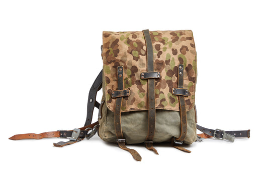 Camouflage-patterned backpack with leather straps on a white background
